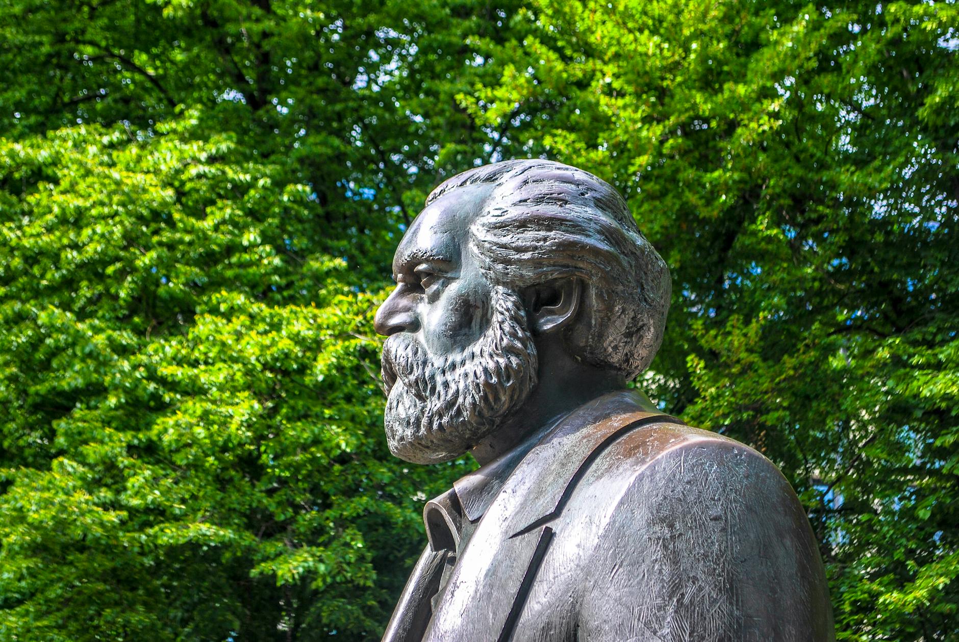 bronze statue of a bearded man and green tree in background